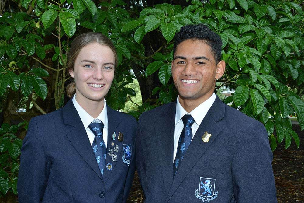 When Denzel Robertson started Mt Albert Grammar School he was “a short, skinny, brown kid who had the same Sonny Bill haircut as every other Polynesian boy”. This week, as head boy, he devoted part of his farewell speech to remember those first few days at Mags in a class full of strangers who soon became his brothers. “ I had a lot of ‘first time’ experiences… like the first time I ever got lost in a school and the first time I’d ever seen cameras in the toilets. The first time I wore Roman sandals and the first time I had to pull my socks up to my knees. “… The first time I shaved and the first time I was ever called a walking billboard. The first time I met my boys, and the first time I was a part of something big… the MAGS family. “ Denzell looked to the pupils of the past and himself and fellow school-leavers of the future when he told the assembly: “Whether you’re in the library studying by yourself or even just at the bar drinking by yourself, you will always have a friend when there’s an Albertian around. Being a part of the MAGS community is both an honour and a privilege as we are a family, and families look after each other.” He thanked teachers for their role in his development and had some special words for his parents: “You taught me to always aim high and to give it my best. To always push myself, as you believed that there is always room for improvement, and to surround myself with great people who I aspire to be like.” Head girl Jaimee McLaughlan said in her speech she had loved every minute at the school – “It has given me great pride to say I am student at Mt Albert Grammar and I look forward to being able to say I am an Albertian”. Jaimee thanked headmaster Patrick Drumm for “believing in me, trusting me to lead this school and for all the early morning coffees”. She also paid tribute to teachers and fellow prefects… and her parents “for your infinite support and love”. The speeches were made at the senior prize-giving, where Lucas Peterson and Harshita Nayyar were named as school dux. They are pictured here with Patrick Drumm.